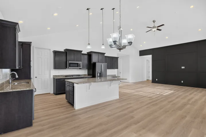 Vaulted ceilings with recessed lighting, wood-finish flooring, dark cabinetry, and a kitchen island with pendant lighting