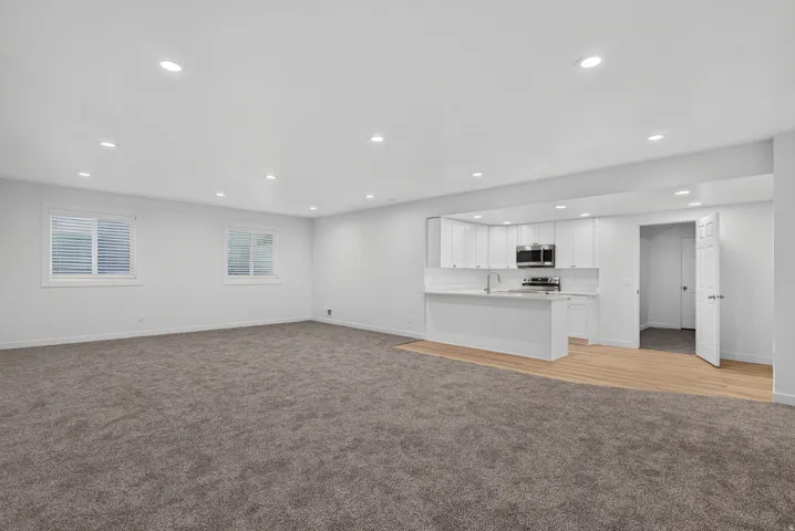 Recessed lighting throughout, white kitchen cabinetry with a stainless steel microwave and range, and light wood-finish flooring