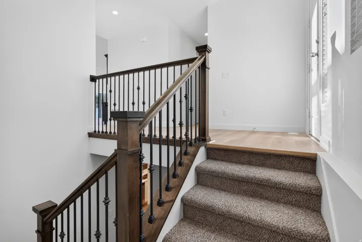 Staircase featuring dark wood newel posts and handrails, black iron balusters, and carpeted treads