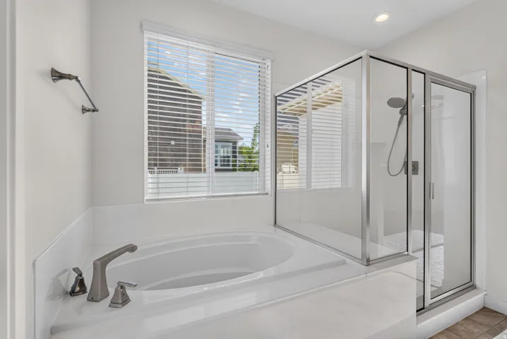 Built-in soaking tub with brushed nickel fixtures, glass-enclosed shower with a handheld showerhead, and a towel bar