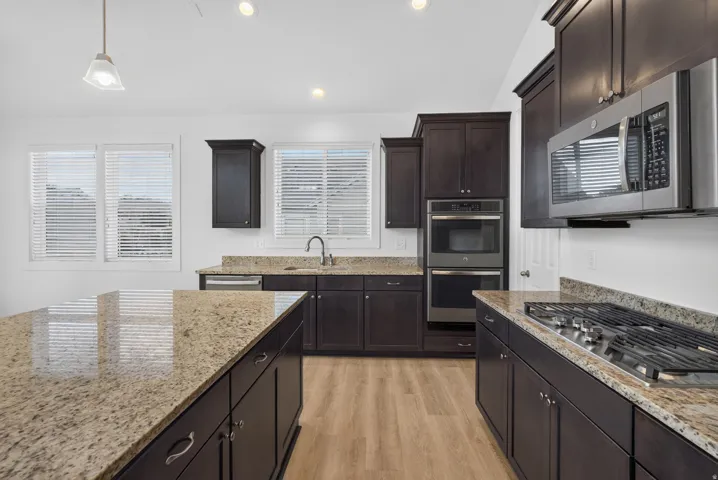 Kitchen featuring rich wood-finish cabinetry, light-toned granite countertops, stainless steel appliances, and wood-finish flooring