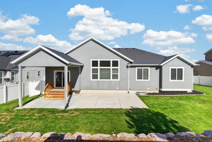 Expansive green lawn, concrete patio, covered porch with wood steps, and multiple windows