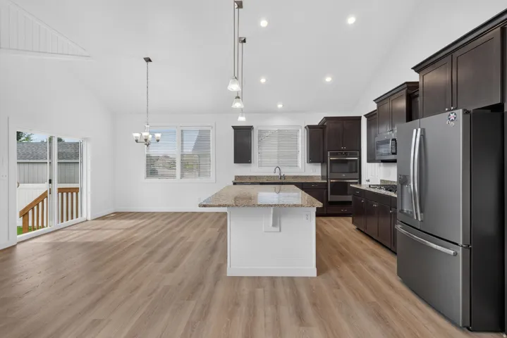 Vaulted ceiling, wood-finish flooring, dark wood cabinetry, stainless steel appliances, and granite countertops