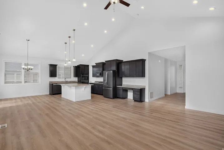 Vaulted ceiling with recessed lighting, wood-finish flooring, dark wood cabinetry, stainless steel appliances, and a kitchen island with a light-toned countertop