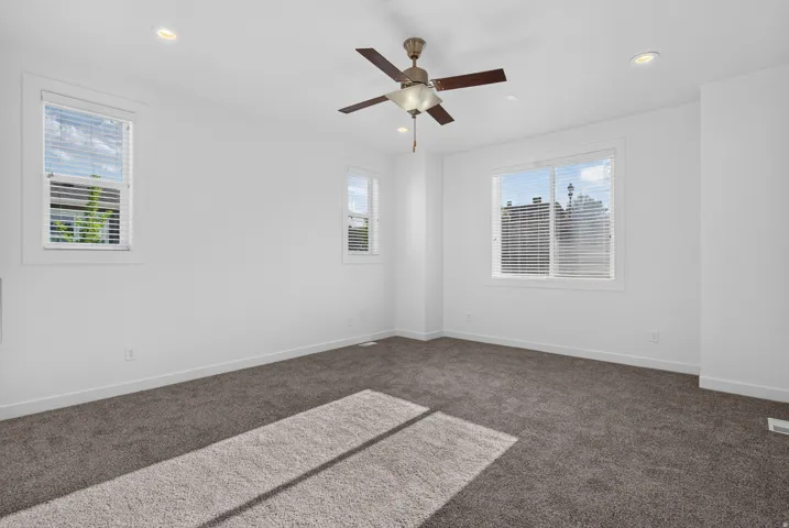 Spacious room featuring neutral carpet, recessed lighting, a ceiling fan, and multiple windows with blinds