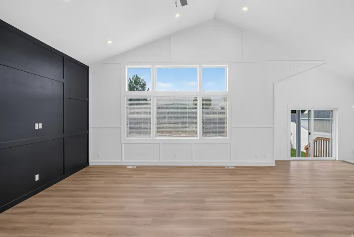 Vaulted ceiling with recessed lighting, large pane windows, wood-finish flooring, accent wall with panel detailing, and a sliding glass door