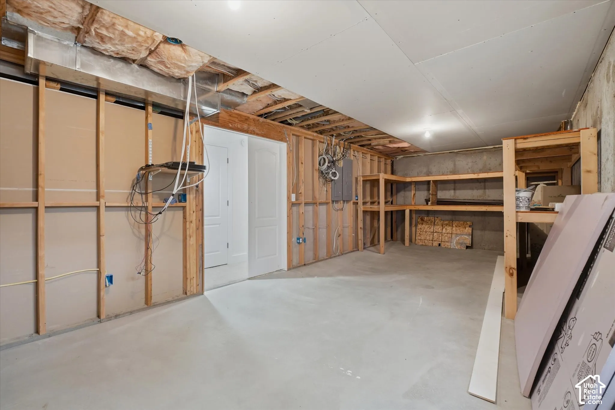 Unfinished lower level with wood framing, exposed insulation, cement flooring, and built-in wood shelving
