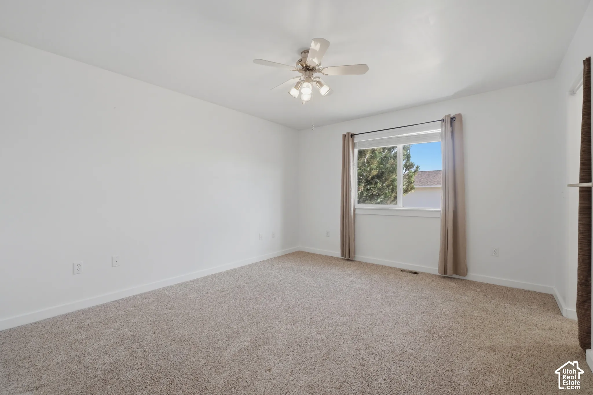 Neutral-toned carpeting, white walls, white window trim, and a ceiling fan with integrated lighting