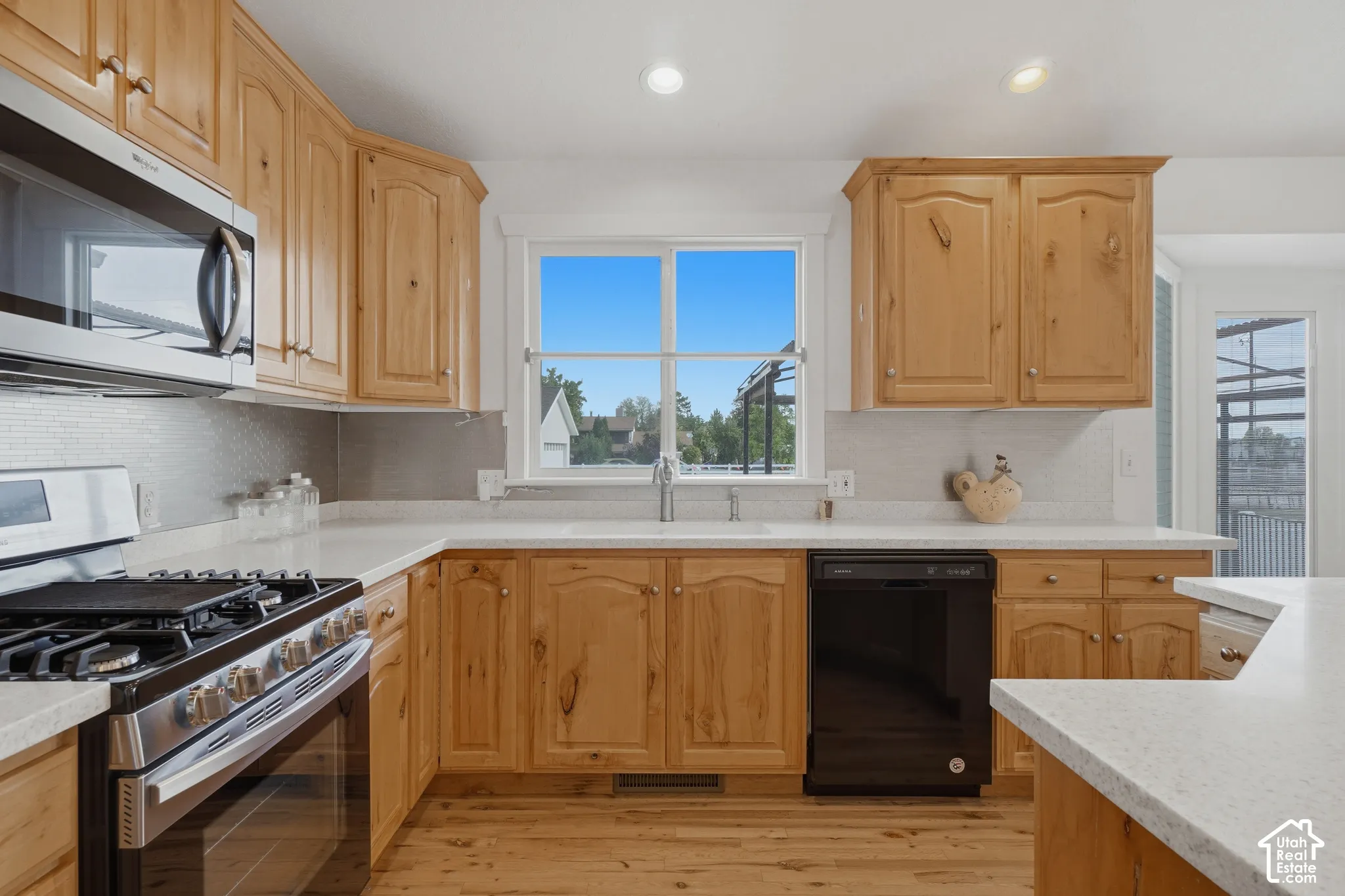 Bright kitchen featuring warm wood cabinetry throughout, stainless steel gas range and built-in appliances, white quartz countertops, and a large center island