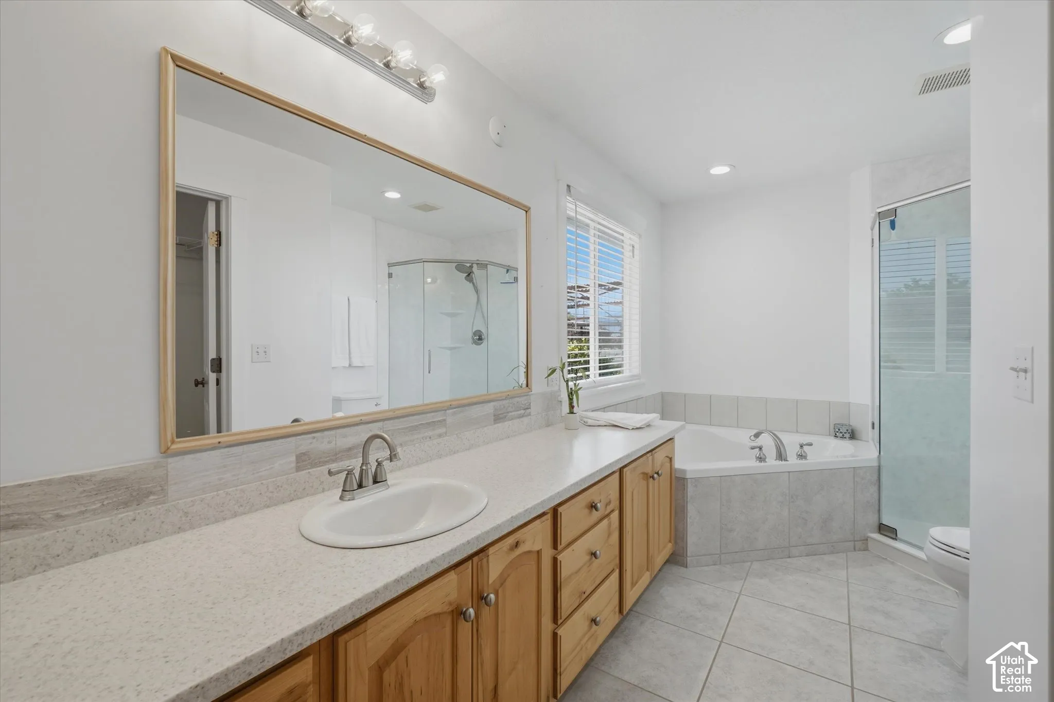 Spa-inspired primary bathroom featuring a wood-finish vanity with dual sinks, quartz countertops, and an expansive framed mirror with integrated lighting