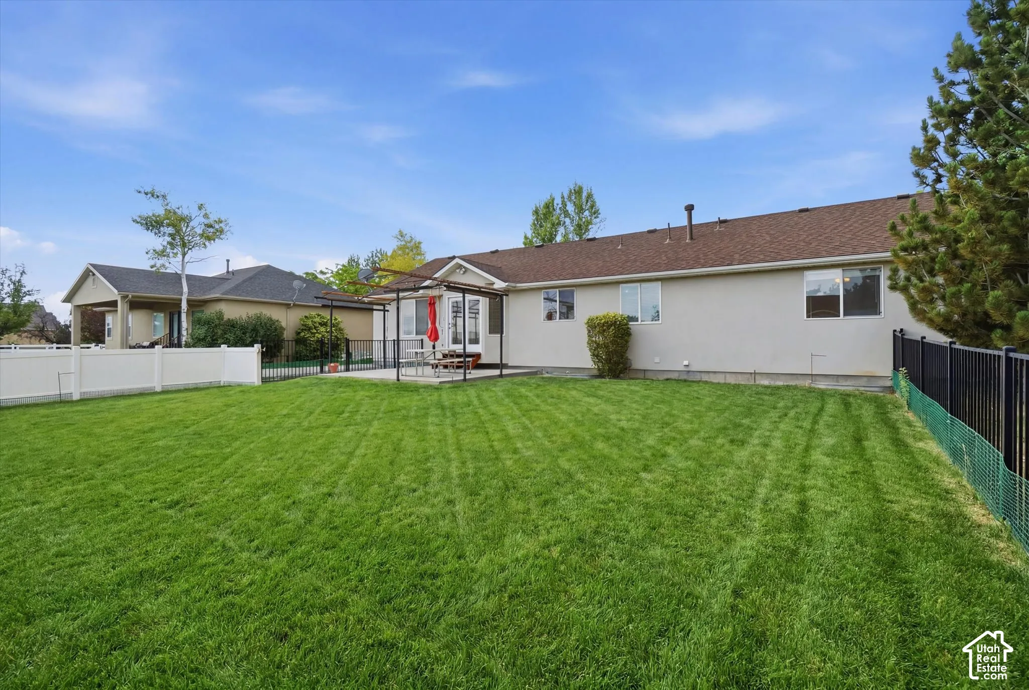 Expansive backyard featuring a manicured lawn, a concrete patio, and a white vinyl privacy fence