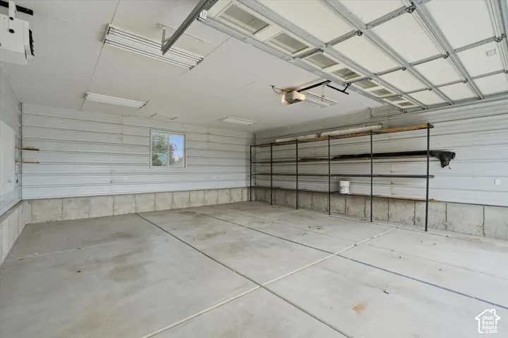 Spacious garage featuring a concrete floor, corrugated metal walls, built-in shelving, and a window for natural light