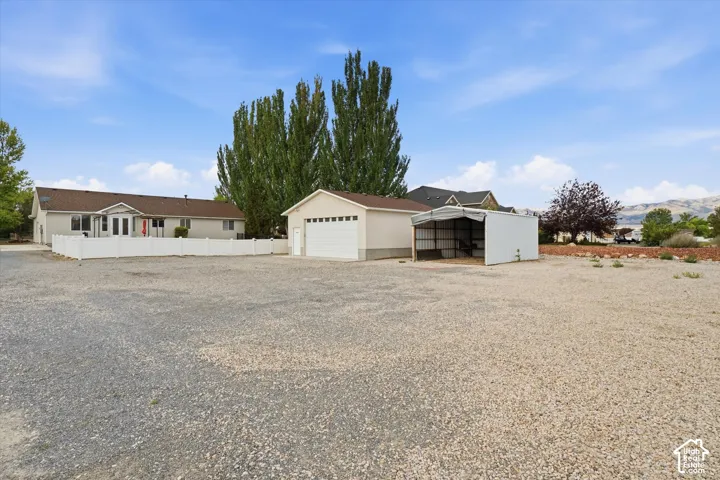Expansive gravel lot featuring a detached garage, white vinyl fencing, and an open-sided metal carport