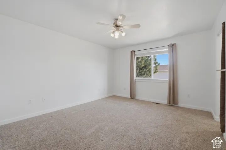 Neutral-toned carpeting, white walls, white window trim, and a ceiling fan with integrated lighting
