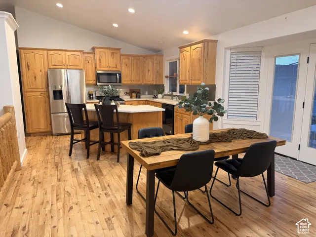 Natural wood-finish flooring, vaulted ceiling, recessed lighting, double French doors, and a kitchen island with seating