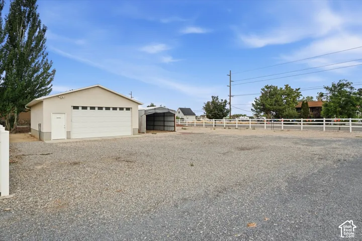 Detached garage with a roll-up door and side entry, paired with an open-sided metal structure, all situated on a gravel surface
