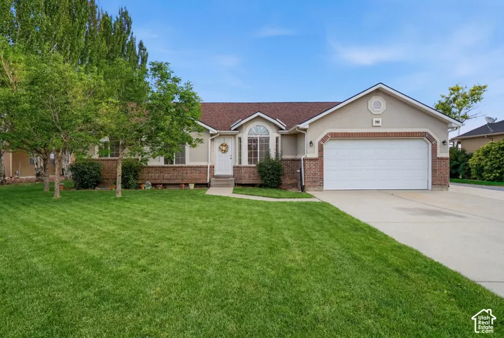 Stucco exterior with brick accents, arched window, attached garage, concrete driveway, and established front landscaping