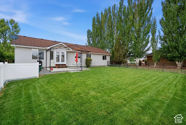 Expansive lawn area, concrete patio, double glass doors, privacy fencing, and mature trees