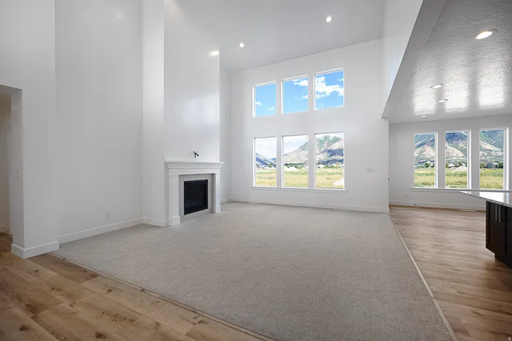 High ceilings with recessed lighting, a fireplace with a white mantel, large windows, and a combination of carpet and wood-finish flooring