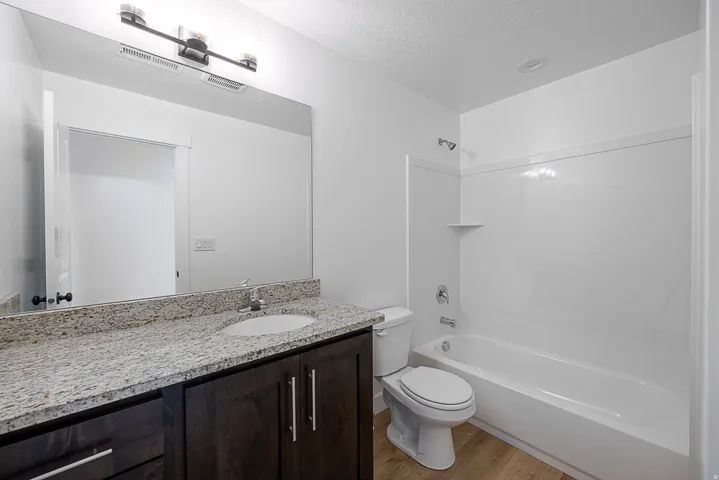 Bathroom featuring a spacious vanity with a light-toned countertop, a rectangular undermount sink, dark wood-finish cabinetry, a large wall-mounted mirror, and a white bathtub with an integrated shower