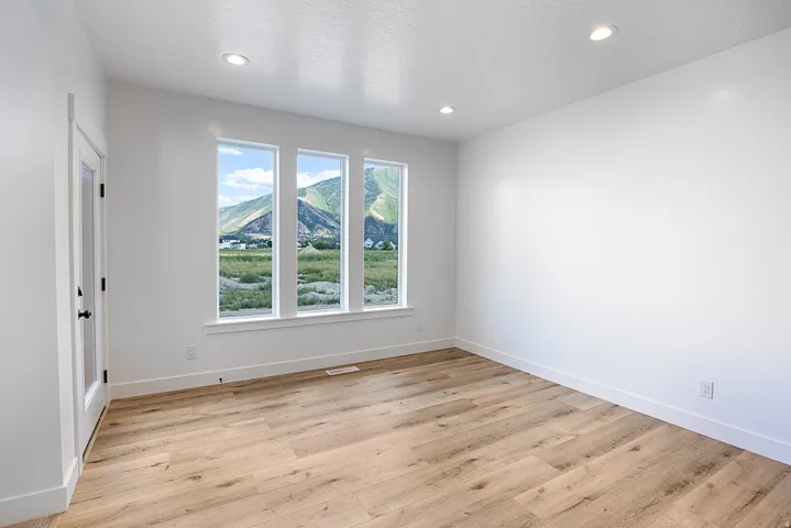 Recessed lighting illuminating a room with wood-finish flooring, a glass-paneled door, and a wall of three windows overlooking a mountain landscape