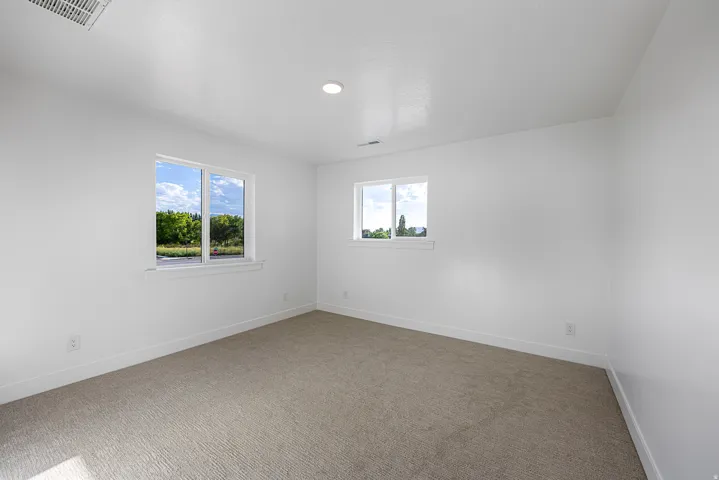 Neutral tone carpeting with white walls, two windows, and recessed lighting