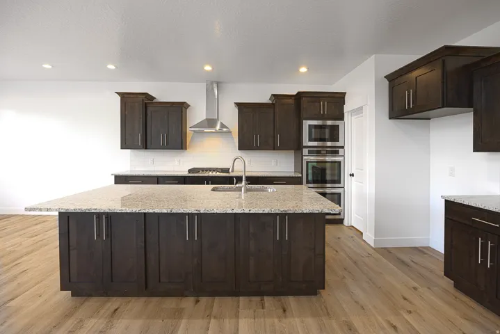 Spacious kitchen with a large central island, wood-finish flooring, dark wood cabinetry, light-toned countertops, and stainless steel appliances