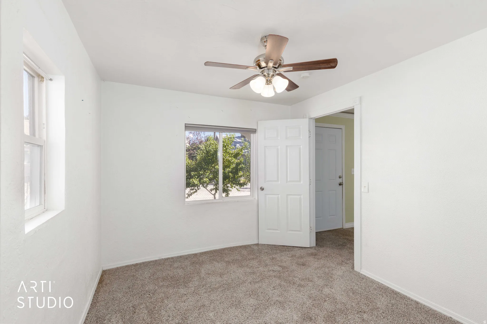 Plush carpeted flooring, two windows, and a ceiling fan with integrated lighting