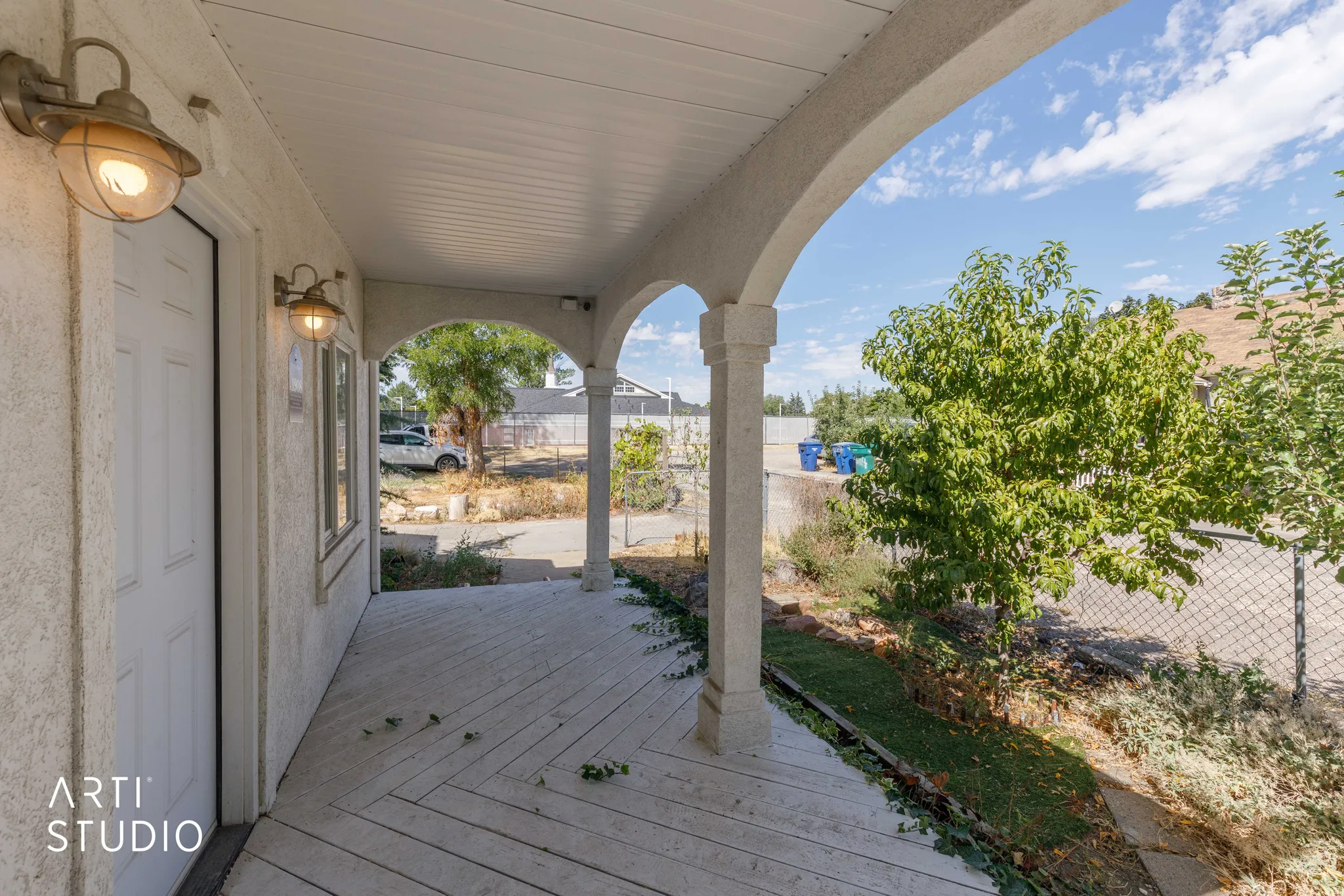 Covered porch with arched supports and ceiling, featuring two wall-mounted outdoor light fixtures, and a textured exterior wall