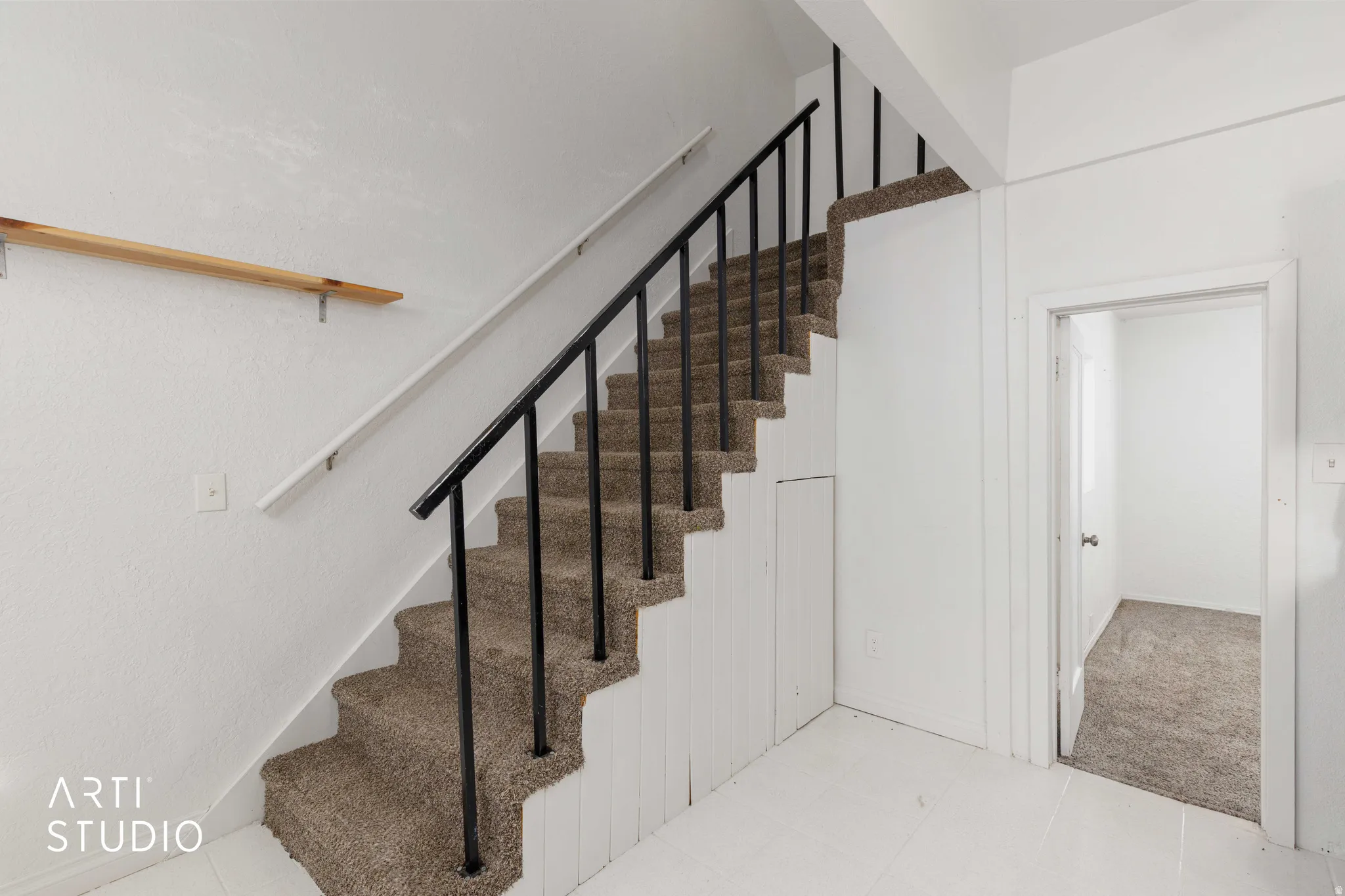 Carpeted staircase with dark metal balusters, white handrail, and white paneled walls