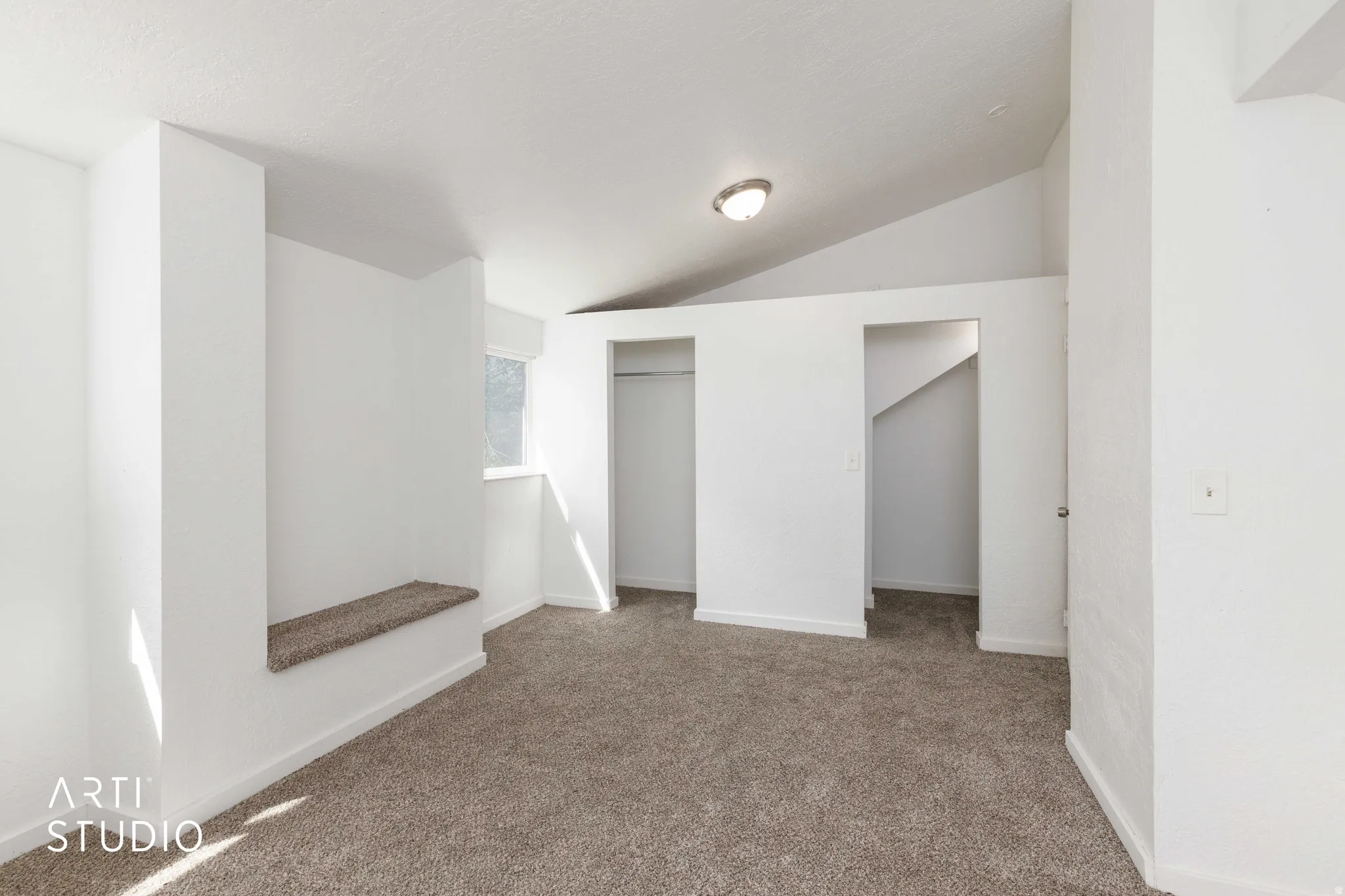 Vaulted ceiling, wall-mounted light fixture, built-in carpeted bench, window, and wall-to-wall carpeting