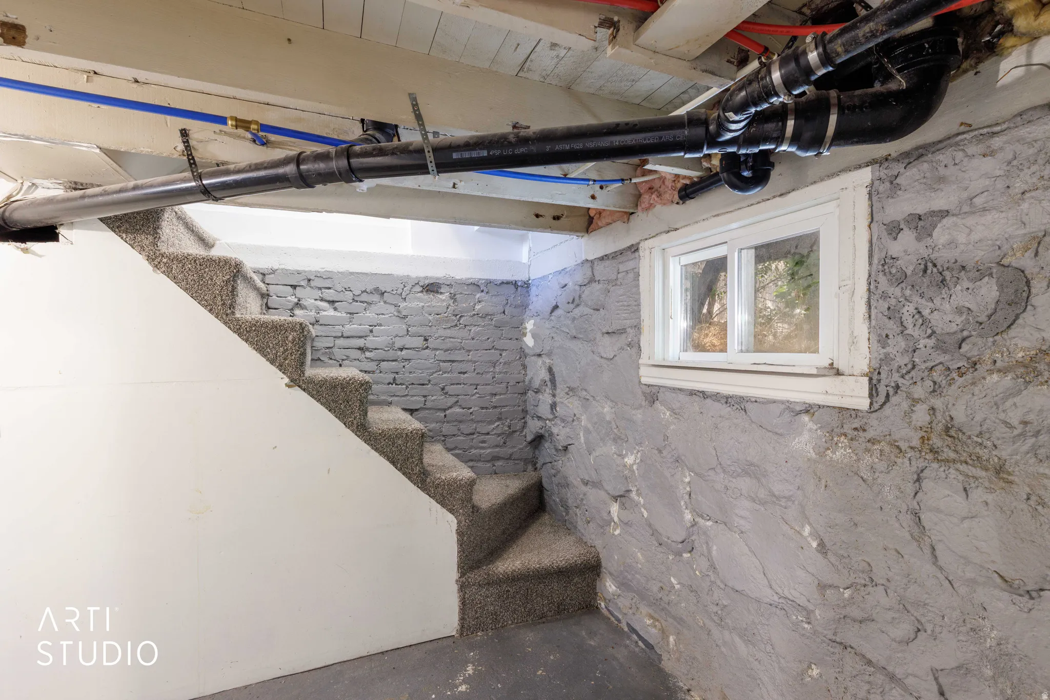 Carpeted stairs leading to a lower level, featuring exposed stone walls and a single-pane window