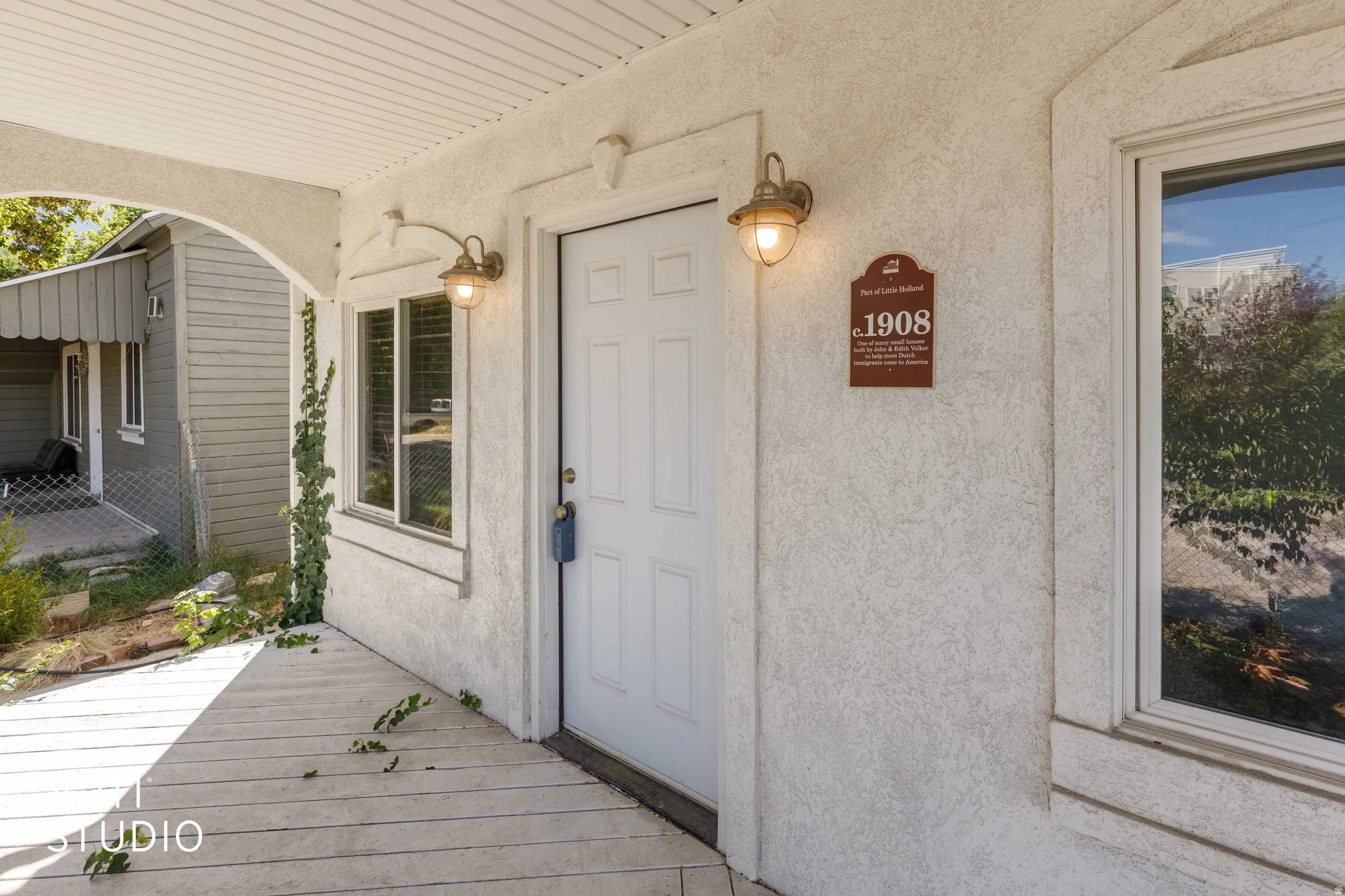 Covered porch entry featuring a paneled door, two exterior sconces, and a window with trim