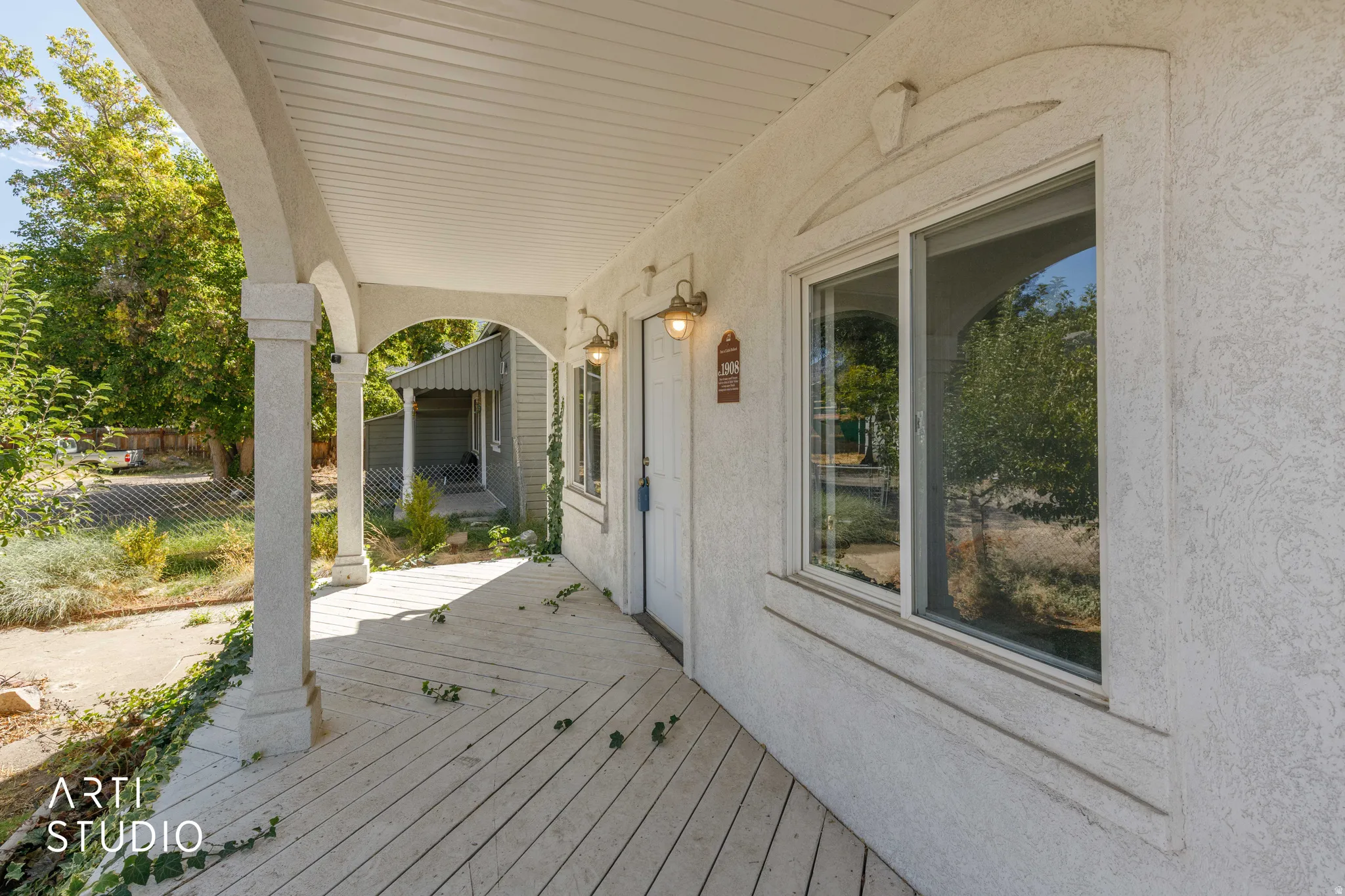 Covered porch with white wood-finish decking, stucco exterior, decorative window trim, and exterior wall sconces