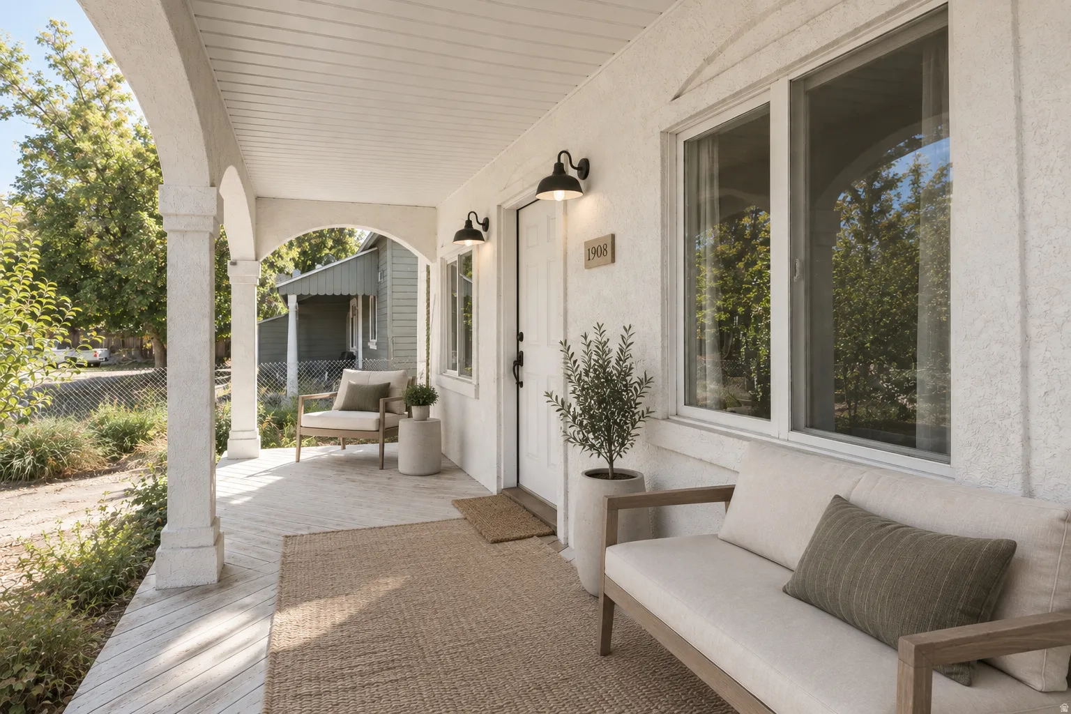 Covered front porch with arched supports, white exterior finish, and wall-mounted exterior lighting