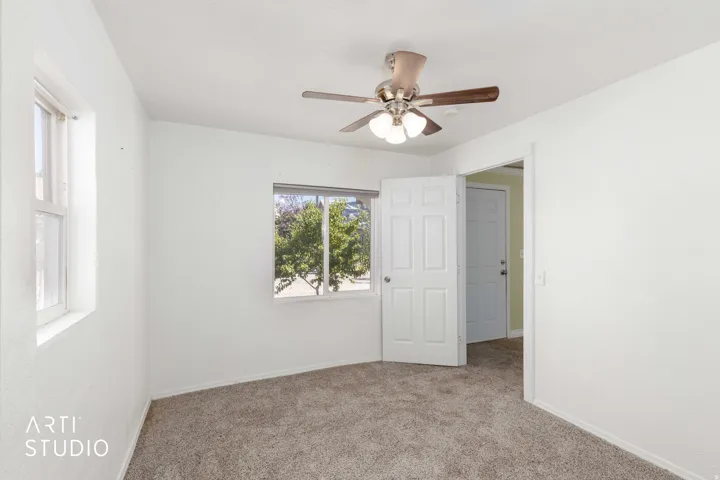 Plush carpeted flooring, two windows, and a ceiling fan with integrated lighting
