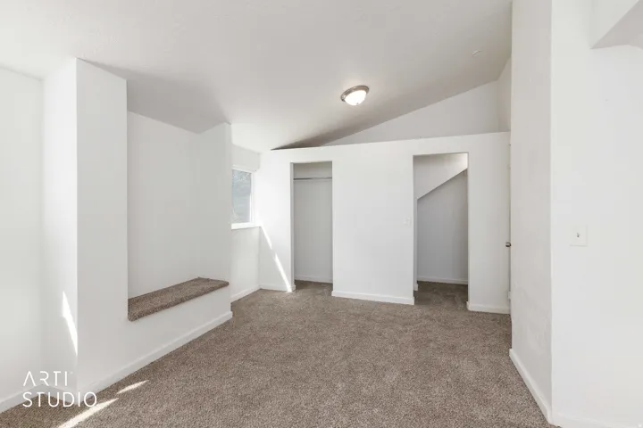 Vaulted ceiling, wall-mounted light fixture, built-in carpeted bench, window, and wall-to-wall carpeting