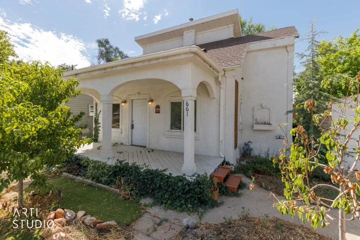 Arched porch entry, column accents, front porch with wood-finish flooring, stucco exterior, and mature trees