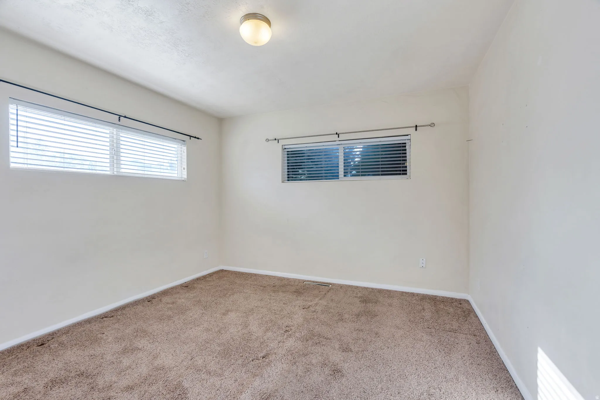 Carpeted room with multiple windows, horizontal blinds, and a ceiling-mounted light fixture