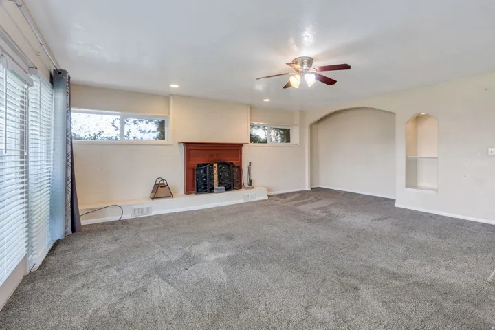 Spacious room featuring a fireplace with a wood mantel, recessed lighting, a ceiling fan, an arched wall niche with shelving, and large windows