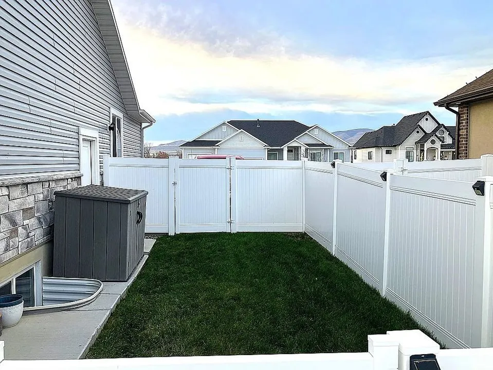 Dog run, white vinyl privacy fencing with gate, manicured lawn, concrete pathway, and a stone-clad foundation