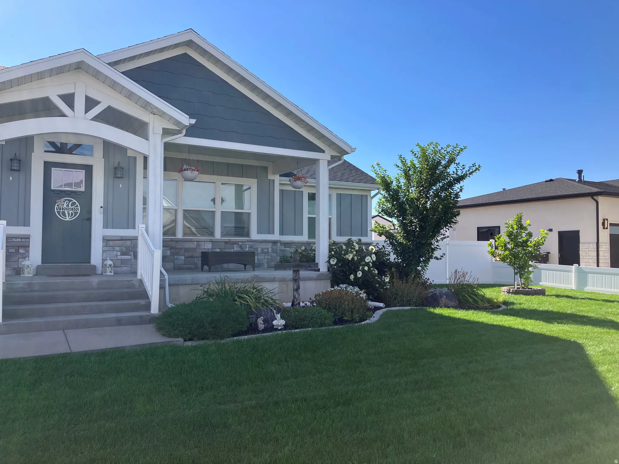 Front exterior featuring a covered porch, stone veneer accents, multi-pane windows, and a landscaped front yard with a white picket fence