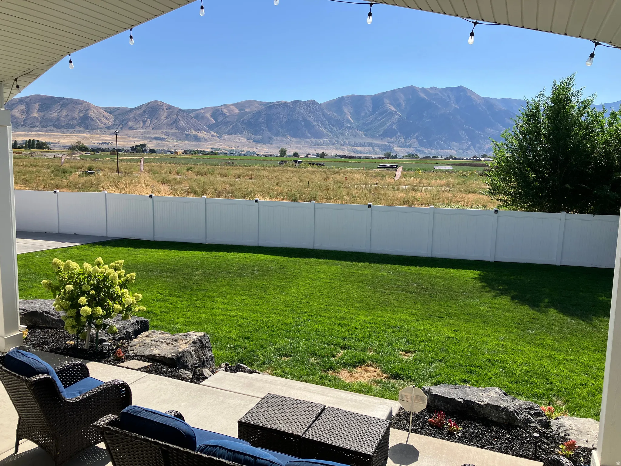 Patio with concrete slab, white privacy fencing, manicured lawn, and mountain scenery