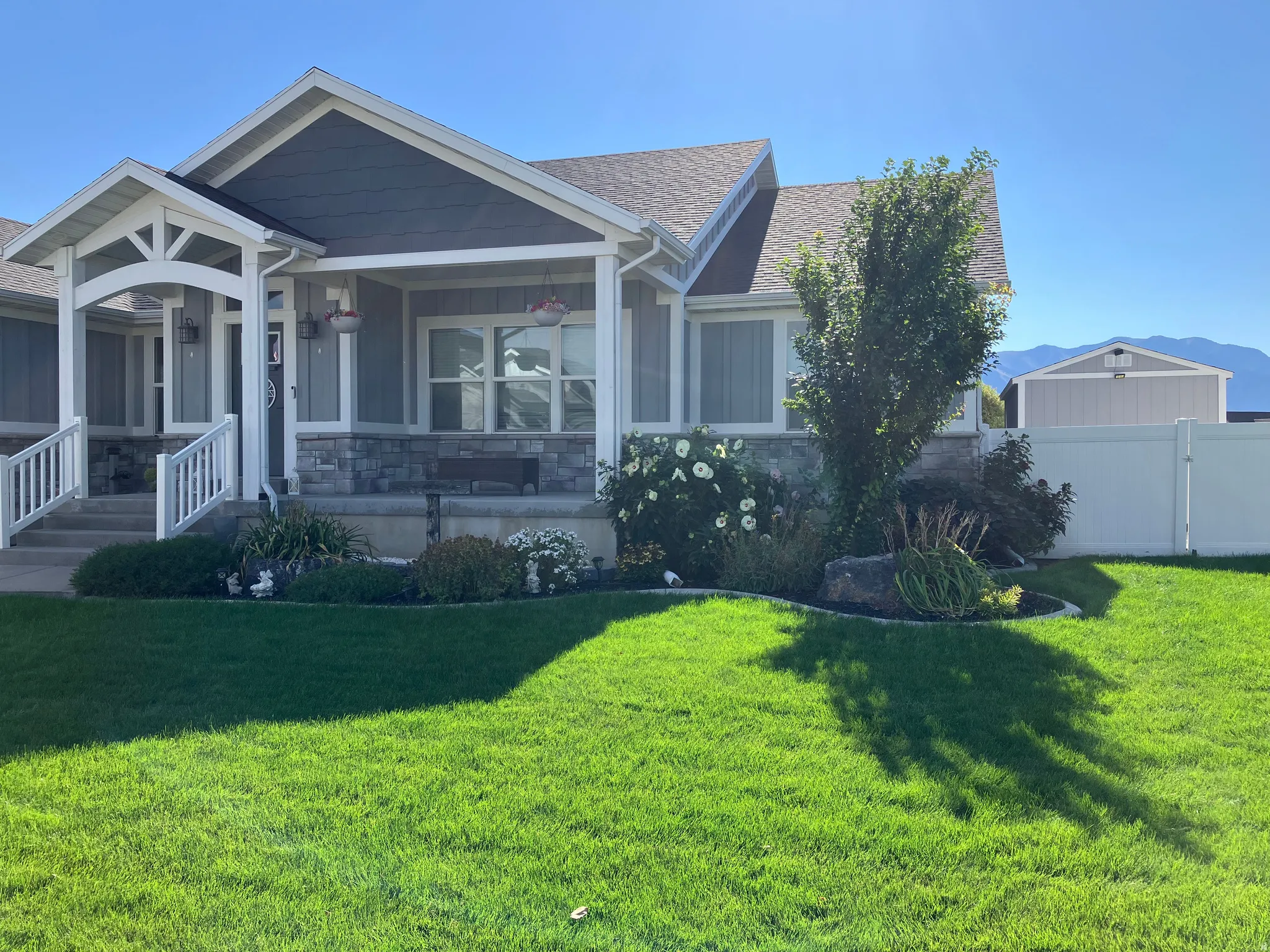 Welcoming porch with stone accents, mature landscaping, and a fenced backyard featuring a shed
