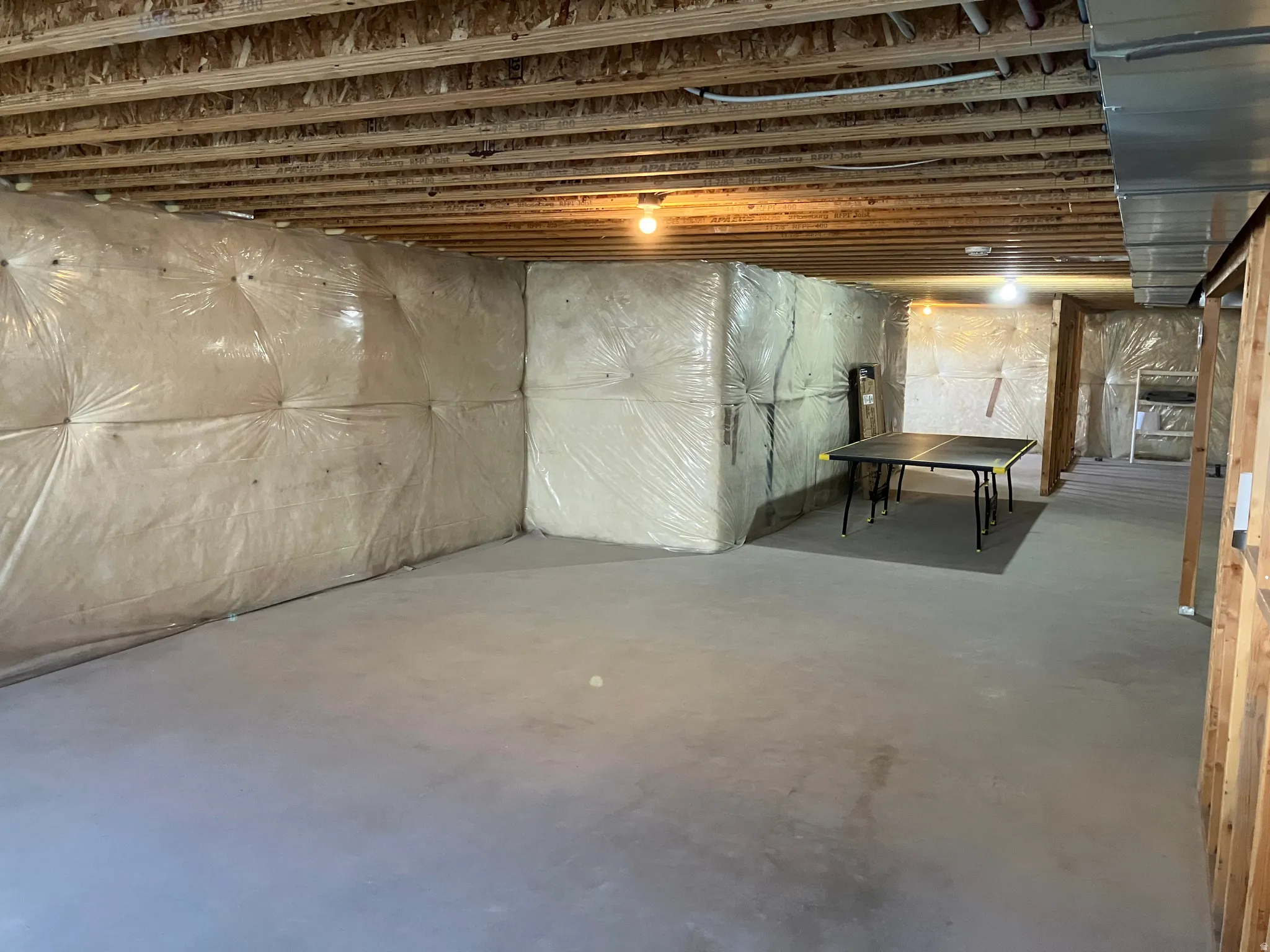 Unfinished basement with exposed joists, concrete flooring, and insulated perimeter walls