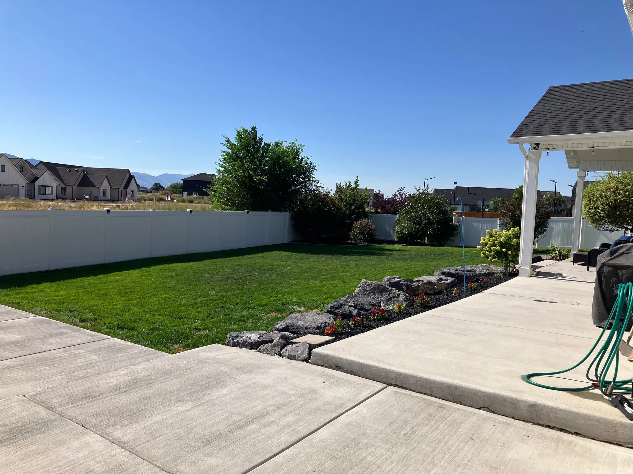 Expansive green lawn with a white privacy fence, concrete patio, and a rock-lined garden bed