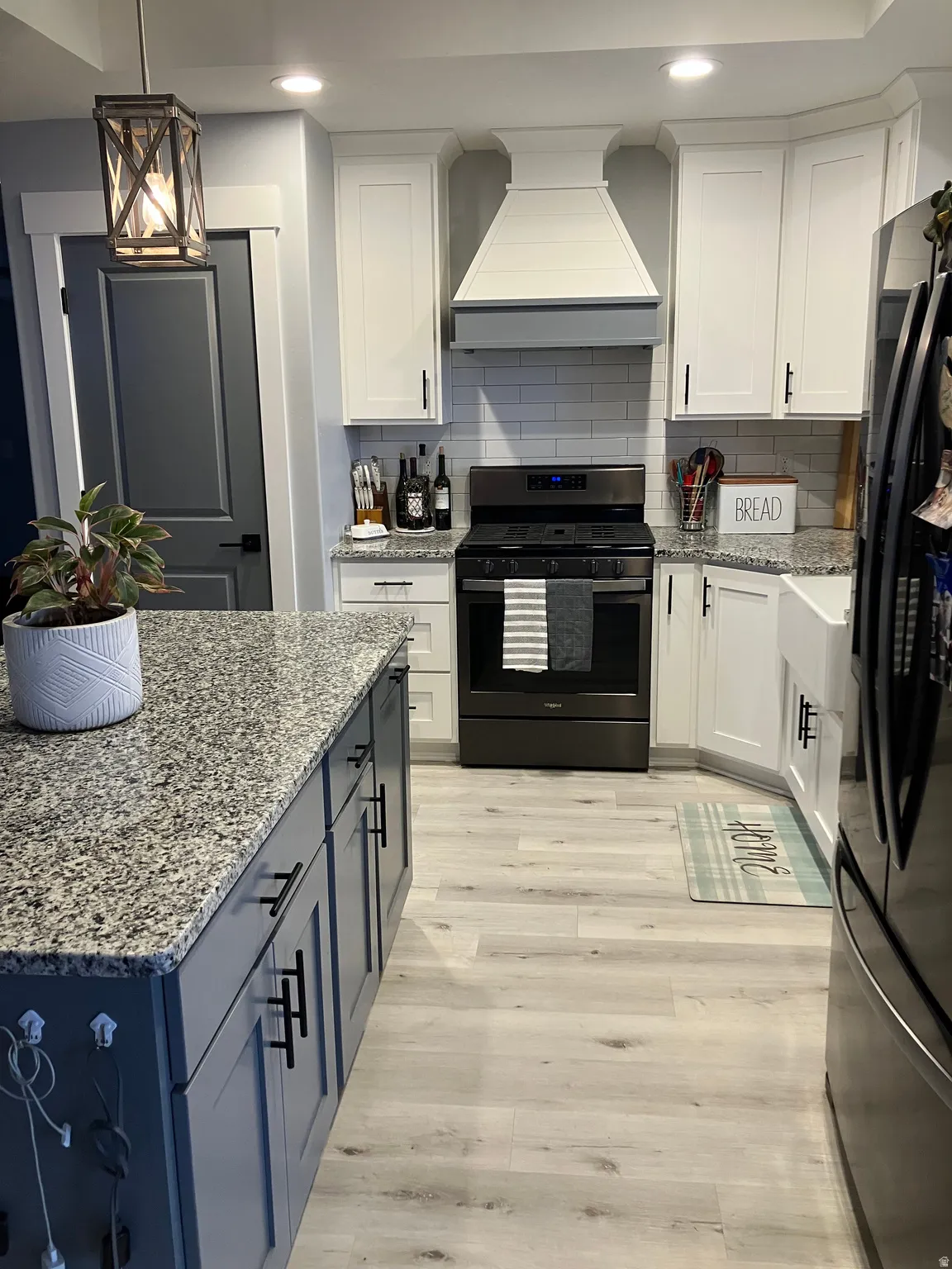 Kitchen featuring a large central island with a granite countertop, white shaker-style cabinetry, subway tile backsplash, and wood-finish flooring