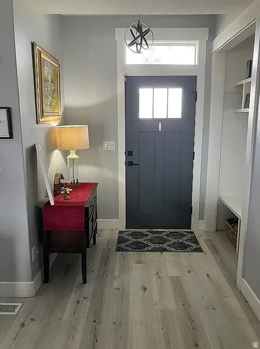 Entryway featuring wood-finish flooring, a dark-paneled door with upper glass inserts, a transom window, and a built-in bench with shelving