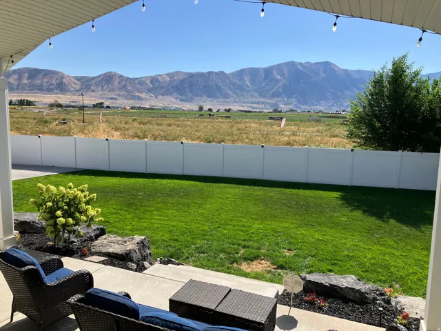 Patio with concrete slab, white privacy fencing, manicured lawn, and mountain scenery