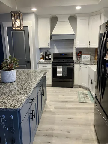 Kitchen featuring a large central island with a granite countertop, white shaker-style cabinetry, subway tile backsplash, and wood-finish flooring